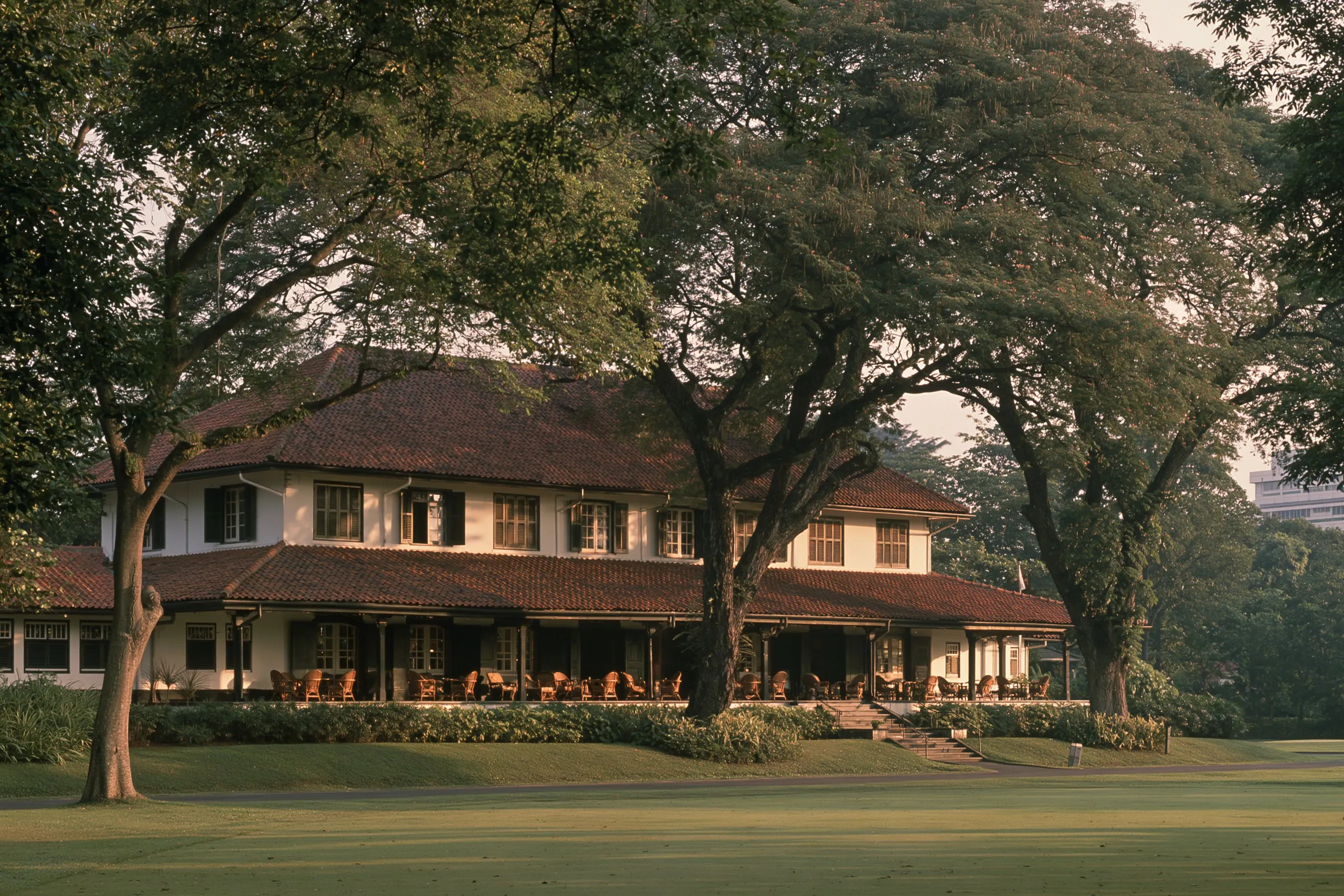 Clubhouse bergaya kolonial dengan beranda dan pohon trembesi tua
