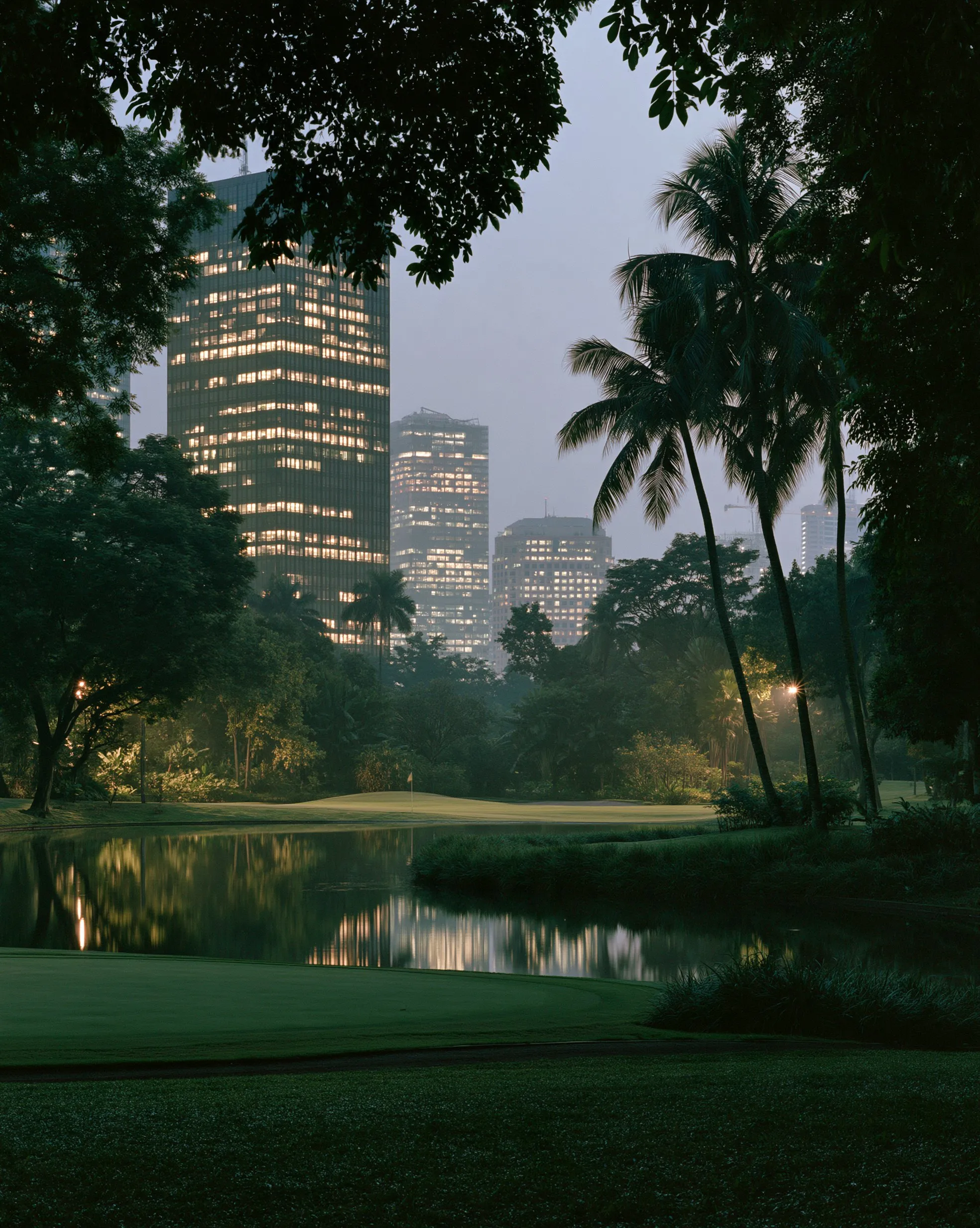 Lapangan golf di Jakarta saat senja dengan gedung-gedung kota di balik pepohonan